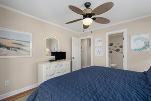A bedroom with a large bed, a ceiling fan, a dresser, and artwork on the walls. - At Ease: Ocean views, short walk to the beach, close to fishing pier. (Nags Head)