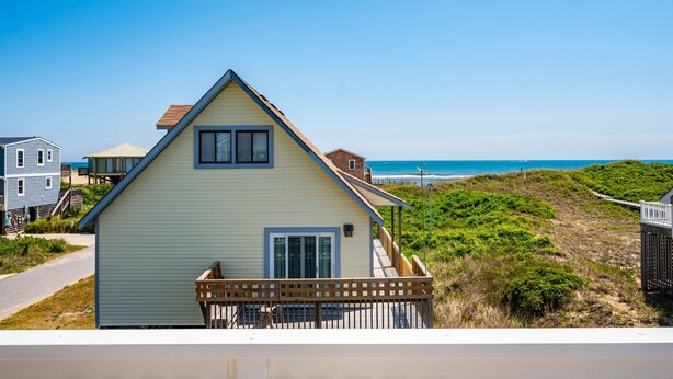 Une maison située sur la côte, dotée d’un balcon, offrant une vue dégagée sur la plage et donnant accès à celle-ci par un sentier.