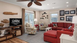 A living room with a television, wicker furniture, a red sofa, and a ceiling fan. - At Ease: Ocean views, short walk to the beach, close to fishing pier. (Nags Head)