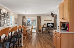 A modern kitchen with wooden cabinets, a dining area with chairs, a ceiling fan, and a television.