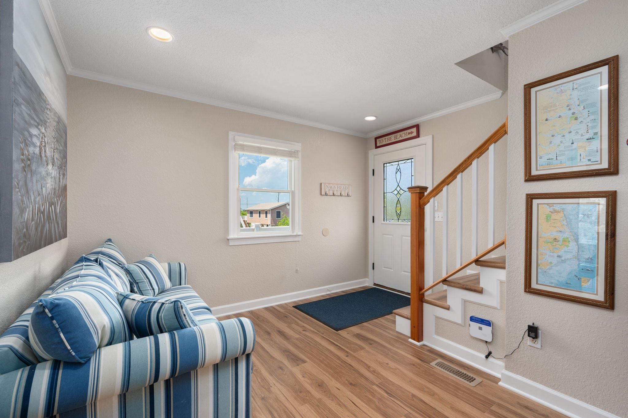A living room with a striped sofa, a wooden staircase, and a door labeled "TO THE BEACH".