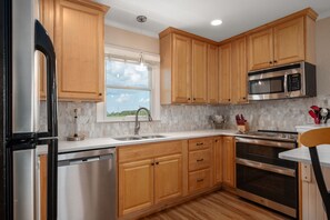 Una cocina con armarios de madera, electrodomésticos de acero inoxidable, un ventanal y vistas al exterior.