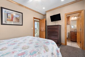 A bedroom with a bed, dresser, television, and a bathroom visible through an open door. - The Sandbox: Oceanfront, private pool, hot tub, rec & theater rooms, elevator! (Kill Devil Hills)