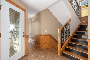 A hallway with a wooden staircase, a glass door with a decorative pattern, and a light fixture on the wall.