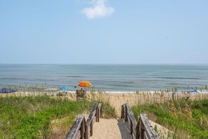 Un sentiero sulla spiaggia che porta verso l'oceano, con ombrelloni e sdraie.