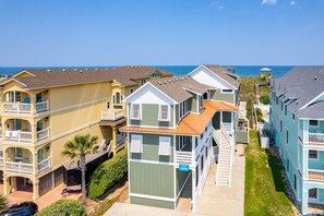 A coastal residential area with multi-story houses, balconies, and a clear view of the ocean. - The Sandbox: Oceanfront, private pool, hot tub, rec & theater rooms, elevator! (Kill Devil Hills)