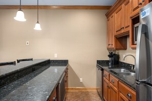 Eine Küche mit Granit-Arbeitsplatten, Holzschränken, einem Edelstahl-Kühlschrank und Pendelleuchten.