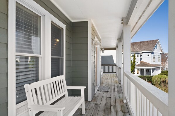 A covered porch with a white bench, a view of a house in the background, and a clear sky.