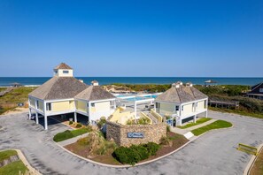 A beachfront property with a swimming pool, multiple buildings, and a stone wall with a sign.