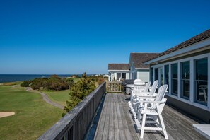 A wooden deck with white chairs overlooking a golf course and ocean view.