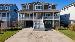 A two-story residential building with a front porch, a staircase leading to the entrance, and a small front yard. - Sunset Shack: Soundfront, great sunsets, hot tub, community pool & tennis courts (Nags Head)