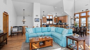 Un salón espacioso con un sofá seccional azul grande, una mesa de comedor de madera y una cocina al fondo.