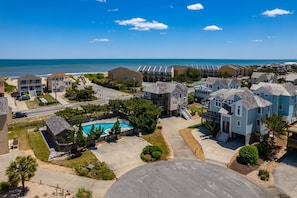 A coastal residential area with a swimming pool, multiple houses, and a clear view of the ocean. - Piggy's Paradise-Oceanside, community pool, private hot tub, short walk to the beach! (Nags Head)