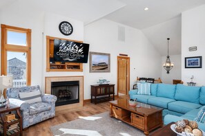 A spacious living room with a fireplace, a large flat-screen TV, a blue sofa, and a wooden coffee table.