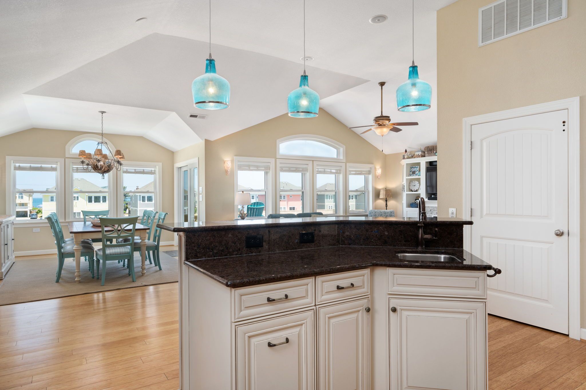 A spacious kitchen with a large island, white cabinetry, and blue pendant lights.