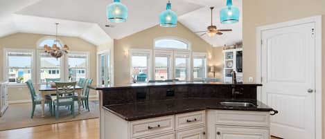 A spacious kitchen with a large island, white cabinetry, and blue pendant lights.