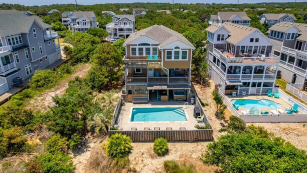 A multi-story residential building with a swimming pool and outdoor seating area. - Beach Brum: Oceanside, private heated saltwater pool, hot tub, elevator, rec room with pool table (Nags Head)