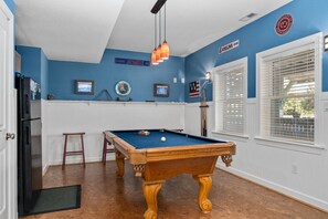 Une table de billard dans une pièce aux murs bleus, aux boiseries blanches et au plancher en bois.