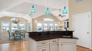A spacious kitchen with a large island, white cabinetry, and blue pendant lights. - Beach Brum: Oceanside, private heated saltwater pool, hot tub, elevator, rec room with pool table (Nags Head)