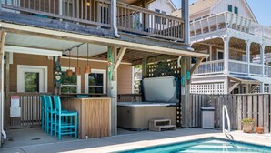 A pool area with a hot tub, wooden deck, and outdoor seating. - Beach Brum: Oceanside, private heated saltwater pool, hot tub, elevator, rec room with pool table (Nags Head)