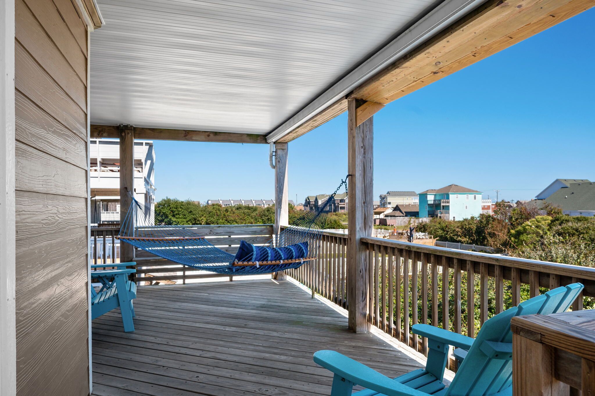 A wooden deck with a hammock and chairs, overlooking a residential area with houses and trees.