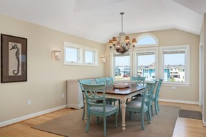 A dining area with a wooden table and teal chairs, a chandelier, and a framed seahorse artwork on the wall.