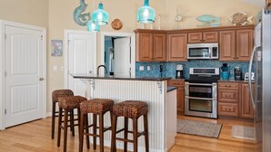 A kitchen with wooden cabinets, a central island with stools, a microwave, and an oven. - Beach Brum: Oceanside, private heated saltwater pool, hot tub, elevator, rec room with pool table (Nags Head)