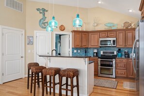 A kitchen with wooden cabinets, a central island with stools, a microwave, and an oven.