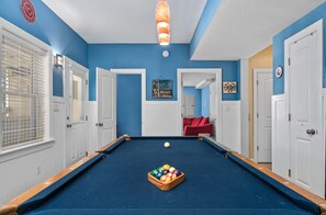 Une table de billard avec des billes, un luminaire au plafond et un panneau indiquant : « Profitez de la plage ».