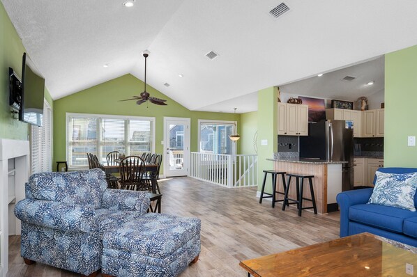 A spacious living area with a high ceiling, a dining area, and a kitchen with a large island.