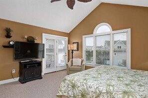 A bedroom with a large bed, a TV, a chair, and a window with blinds.