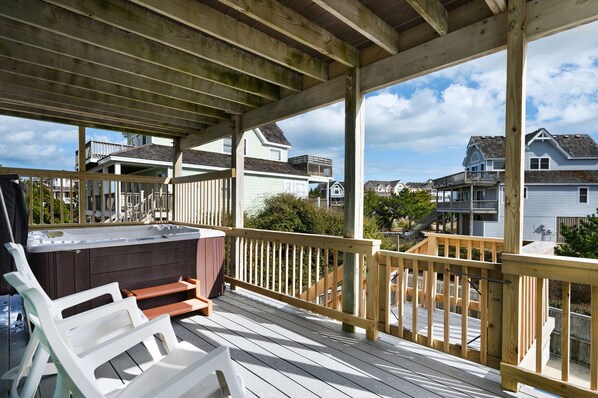 A wooden deck with a hot tub, white lounge chairs, and a wooden railing.
