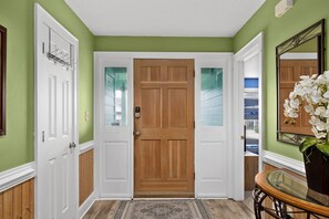 A hallway with a wooden door, white walls, and a glass door leading to a balcony.