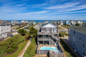 A residential area with a two-story house featuring a balcony, a swimming pool, and a view of the ocean.