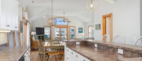 Una cocina amplia con encimeras de granito, armarios blancos y un comedor con sillas y mesa de madera.