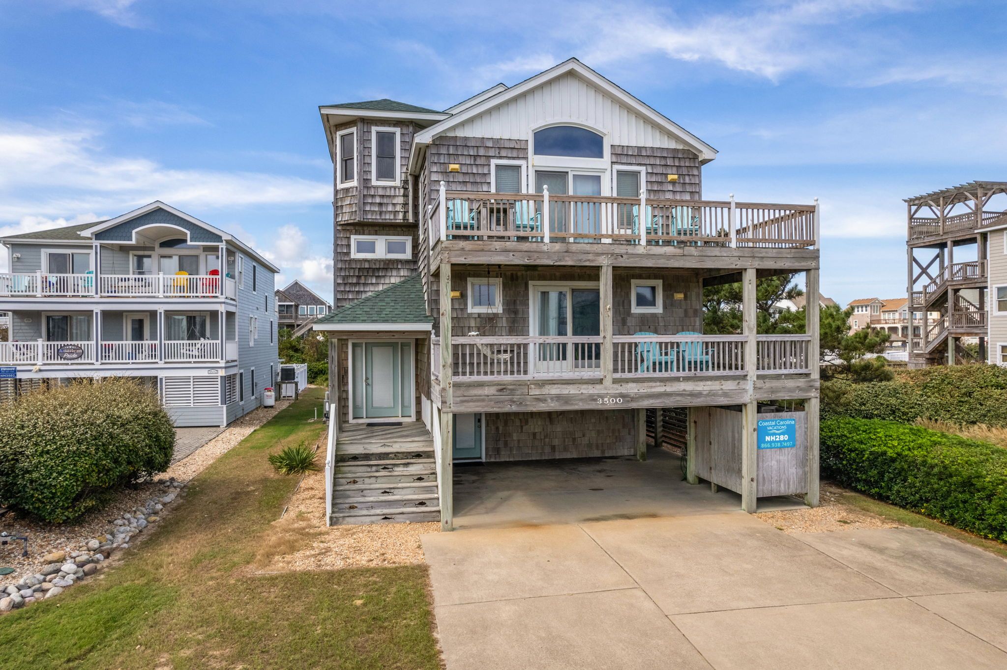 A multi-story coastal building with balconies, a covered front porch, and a clear sky.