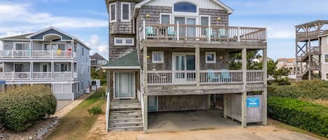 A multi-story coastal building with balconies, a covered front porch, and a clear sky.