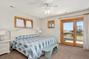 Une chambre à coucher comprenant un lit, une table de chevet, un ventilateur de plafond, une fenêtre avec des rideaux et une vue sur l’extérieur.