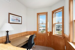 A corner room with wooden paneling, a desk with a chair, a lamp, and two windows with starfish decorations.