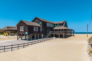 Un bâtiment situé en bord de mer, à plusieurs niveaux, doté d’une terrasse en bois et d’un escalier menant à la plage.