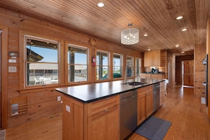 A wooden cabin interior with a kitchen featuring a central island, wooden cabinets, and large windows.