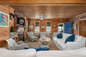 A wooden cabin interior with wicker furniture, a fireplace, and a ceiling fan.