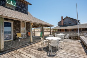 A wooden deck with outdoor seating and a covered area, overlooking a beach.