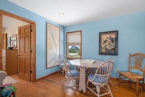 A dining area with a wooden table and chairs, a window with blinds, and a door leading to another room.