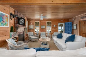 A wooden cabin interior with wicker furniture, a fireplace, and a ceiling fan.