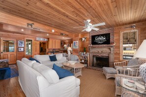 A log cabin interior with a white sofa, blue cushions, a fireplace, a television, and a ceiling fan.