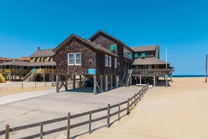 A wooden building with a balcony, a staircase, and a sign indicating a beach location.