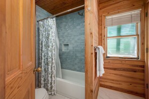 Ein Badezimmer einer Holzhütte mit Dusche, Toilette und einem Fenster mit Jalousien.