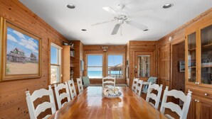 Ein Holzinterieur mit Esstisch, Stühlen, Deckenventilator und großen Fenstern.