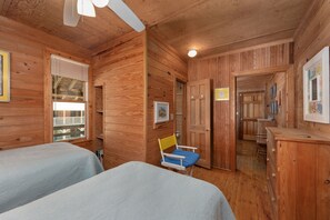 Ein Holzblockhaus-Innenraum mit zwei Betten, einem Sessel, einem Schreibtisch und einer Tür, die auf einen Balkon führt.